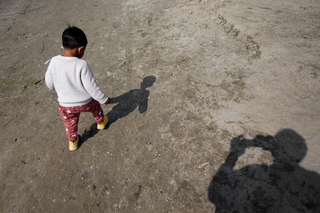 Adorable niño pequeño caminando por la playa de arena con una sombra detrás de él El guardián está capturando las imágenes y las sombras son visibles