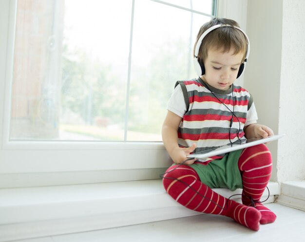 Adorable niño pequeño en casa con tableta y auriculares