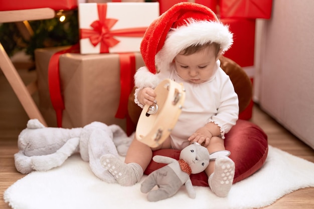 Adorable niño pequeño sosteniendo pandereta sentado en el piso por regalo de navidad en casa