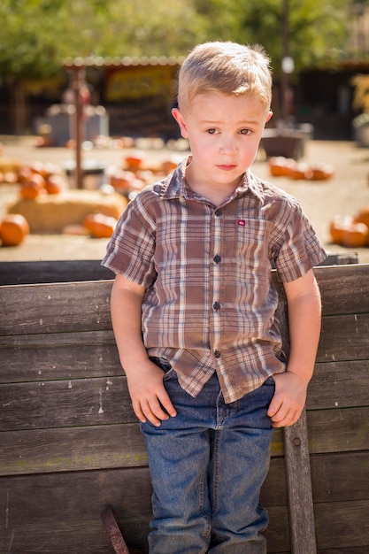 Adorable niño de pie contra un viejo vagón de madera en Pumpkin Patch en un entorno rural