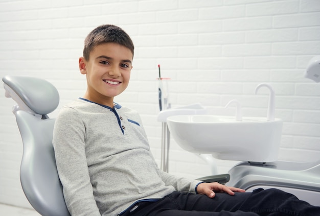 Foto adorable niño preadolescente sentado en la silla del dentista durante la cita dental para el chequeo médico preventivo regular, sonríe con dientes sonrisa mirando a la cámara. concepto de cuidado dental y bucal.