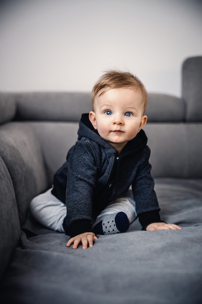 Adorable niño rubio con hermosos ojos azules sentado en el sofá