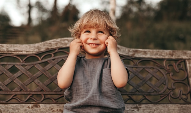 Adorable niño rubio sonriendo y pellizcando las mejillas