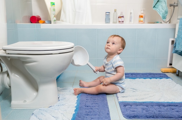 Adorable niño sentado en el piso en el baño.