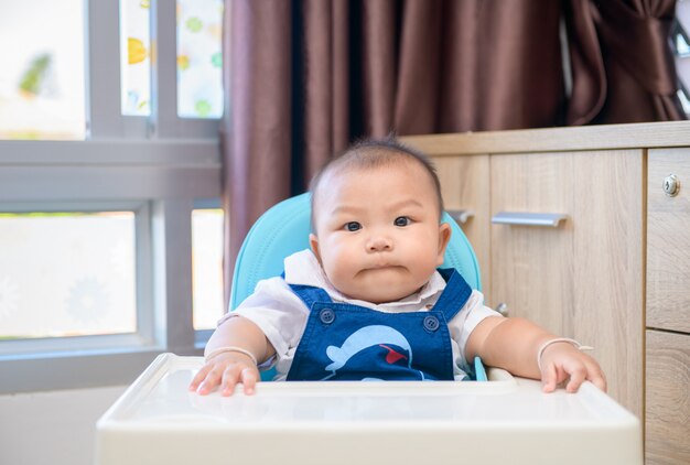 Adorable niño sentado en una silla alta y esperando comida favorita para bebés,