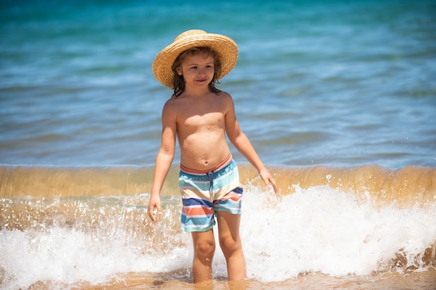 Adorable niño con sombrero de paja en la playa durante las vacaciones de verano retrato de niño juguetón en el mar ...