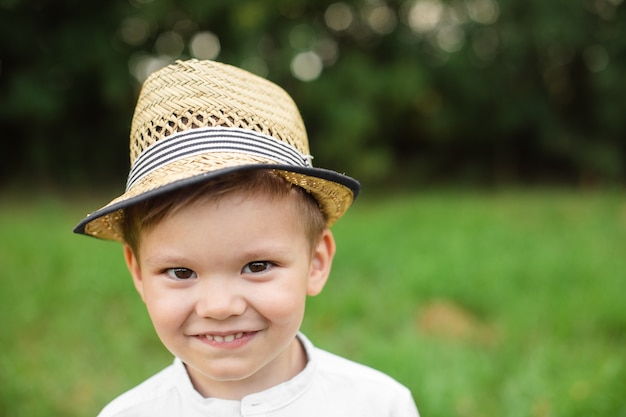 Adorable niño con sombrero de verano. Foto de cabeza de un lindo niño preescolar con sombrero de verano sonriendo felizmente a la cámara contra el fondo borroso del parque.