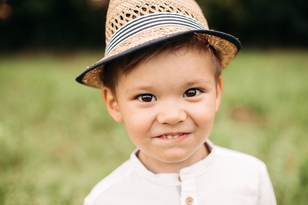 Adorable niño con sombrero de verano. Foto de cabeza de un lindo niño preescolar con sombrero de verano sonriendo felizmente a la cámara contra el fondo borroso del parque.