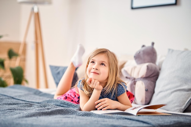 Foto adorable niño sonriente leyendo un libro mientras está sentado en la cama