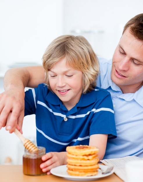 Adorable niño y su padre poniendo miel en gofres