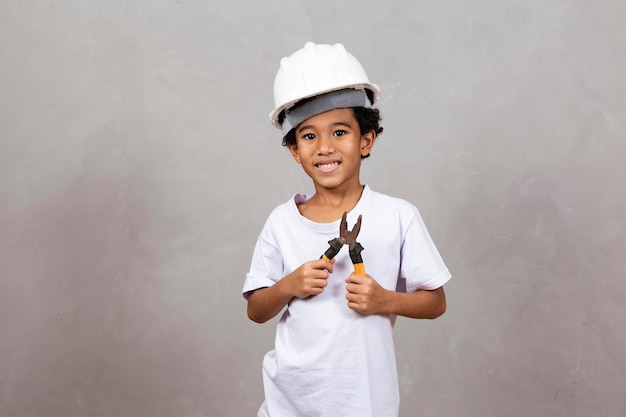 Adorable niño vestido como constructor sosteniendo una herramienta de alicates