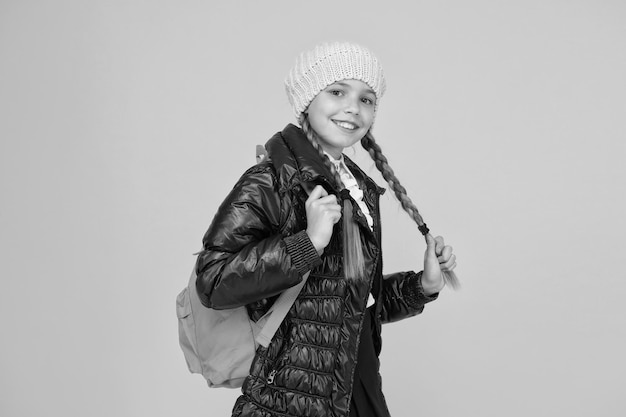 Adorable Schüler Herbst Herbst Winter Kind mit Rucksack Modegeschäft Modekonzept Mädchen tragen Strickmütze und Jacke gelben Hintergrund Kaufen Sie Kleidung für die Schulsaison Schulmädchen-Mode-Outfit