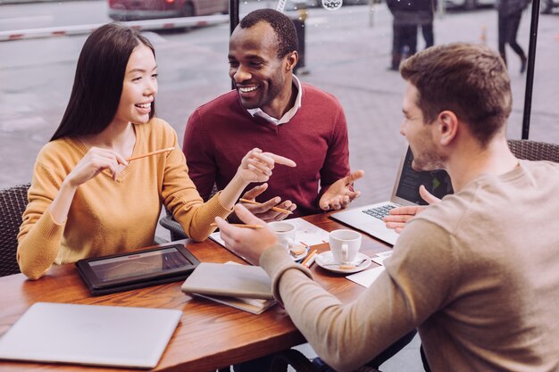 Foto adorables y ambiciosos tres colegas tienen discusión mientras gesticulan y ríen