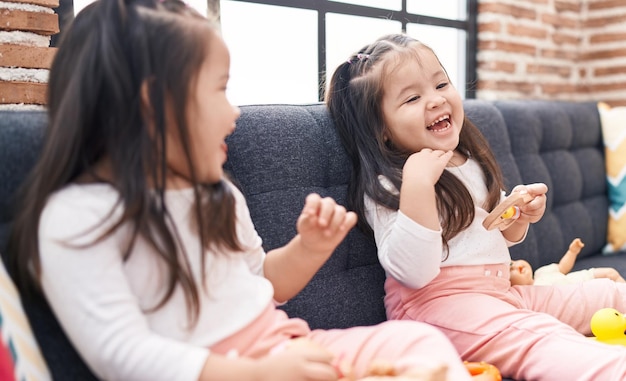 Adorables gemelas sentadas en un sofá sonriendo confiadas en casa