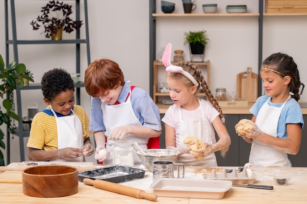 Adorables hermanitas con amplias sonrisas mientras están de pie en la mesa de madera y preparan un refrigerio saludable para sus padres.