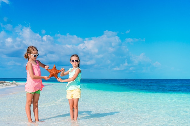 Adorables niñas con estrellas de mar en la playa vacía blanca