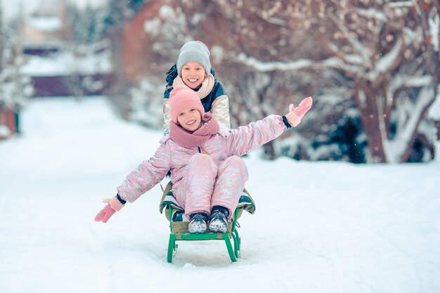 Adorables niñas felices en trineo en día de invierno cubierto de nieve.