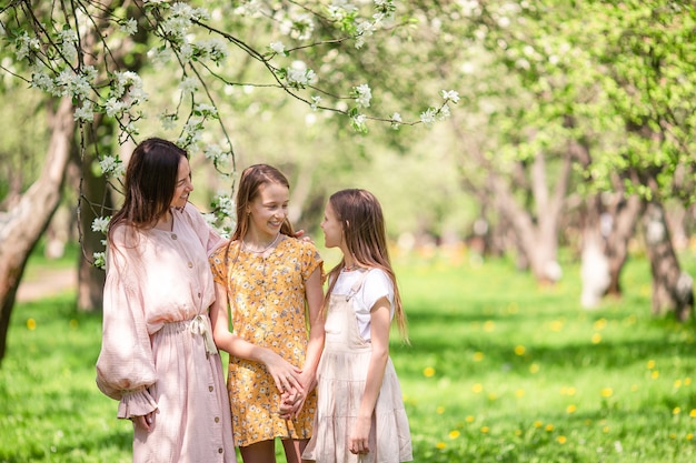 Adorables niñas con madre joven en jardín floreciente de cerezos en el hermoso día de primavera