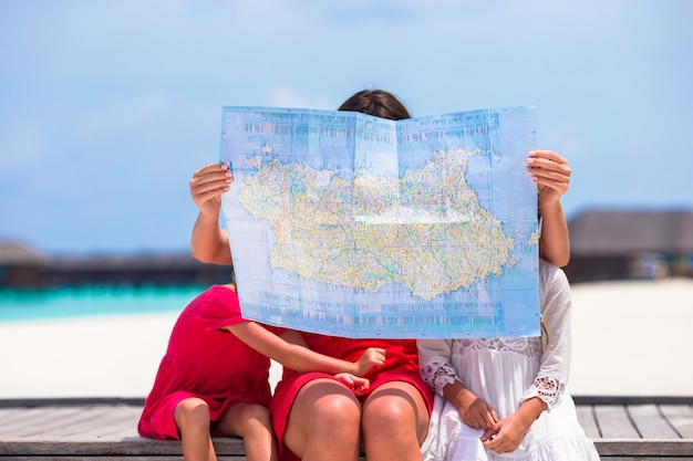 Adorables niñas y mamá con el mapa de la isla en la playa