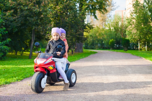 Adorables niñas montando en moto para niños en el parque verde