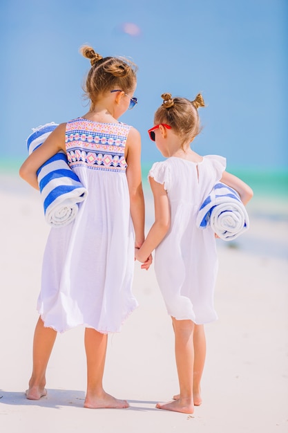 Adorables niñas con toallas de playa en playa tropical blanca