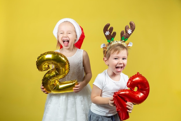 Adorables niños caucásicos sosteniendo globos con números y haciendo muecas