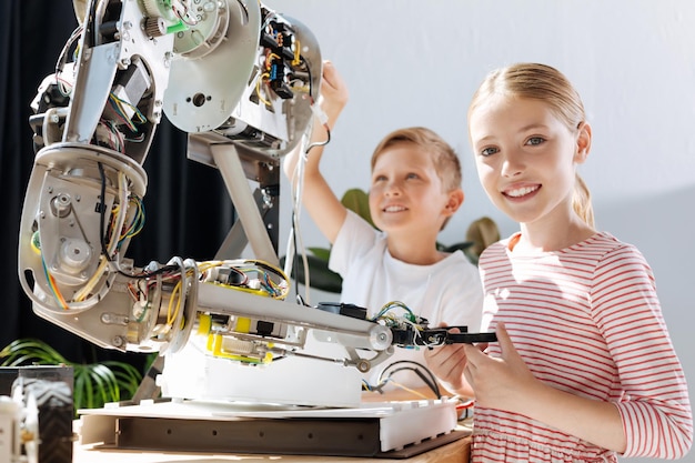 Foto adorables niños preadolescentes inspeccionando el taller de vehículos robóticos