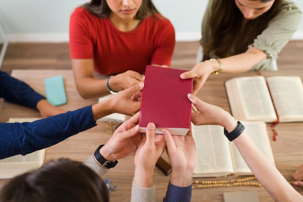 Adoración y fe. Jóvenes católicos tocando y sosteniendo la sagrada biblia mientras rezan en un grupo religioso