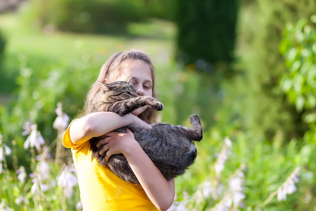 Adorale-Mädchen im gelben Kleid, das reizende Katze in ihren Händen hält. Kind und Haustier draußen am Sommertag.