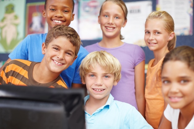 Adoramos a aula de informática Retrato de um grupo de crianças bonitas sentadas e em pé ao redor de um computador durante a aula