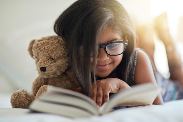 Adoramos a hora da história a qualquer momento Foto de uma garotinha fofa lendo um livro em seu quarto com seu ursinho de pelúcia ao seu lado