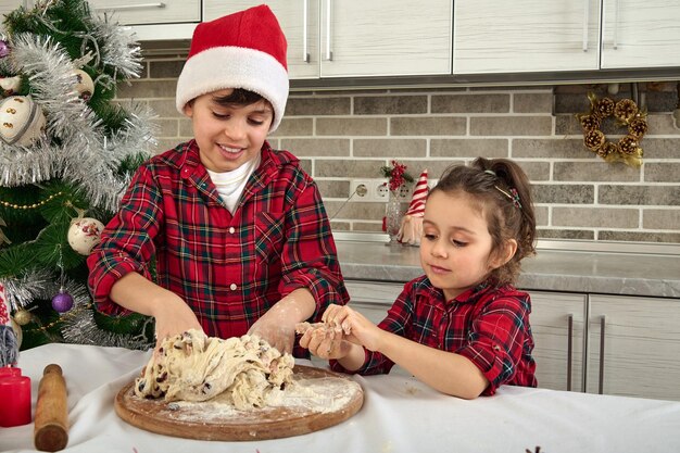 Adoráveis crianças bonitos cozinhando juntos na cozinha de casa durante as férias de Natal. Encantador menino pré-adolescente com chapéu de Papai Noel e sua irmãzinha fofa preparando e amassando massa para fazer pão