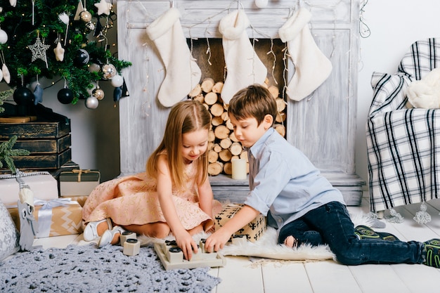 Adoráveis crianças brincando na sala com cristmas árvore e lareira. Conceito de férias de inverno.