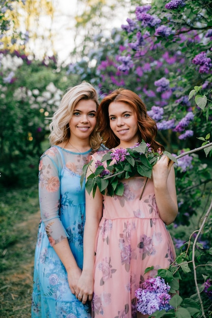 Adoráveis irmãs gêmeas fabulosas alegres felizes adoráveis no verão lindo diferentes vestidos posando no parque primavera florescendo.