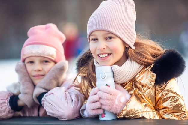 Adoráveis meninas patinando na pista de gelo ao ar livre no dia de neve do inverno