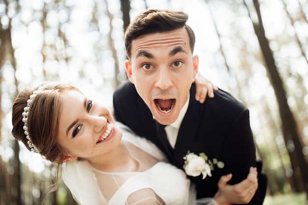 Foto adoráveis recém-casados abraçando e sorrindo em um parque verde. retrato dos noivos em um vestido de renda. dia do casamento de um casal recém-casado feliz