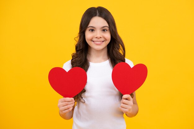 Adorável adolescente romântica segura o símbolo do coração vermelho do amor para o dia dos namorados isolado em fundo amarelo Adolescente feliz, emoções positivas e sorridentes da adolescente