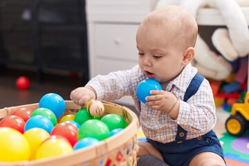 Adorável bebê caucasiano brincando com bolas sentadas no chão no jardim de  infância