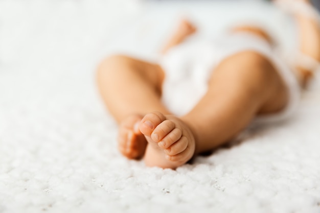 Foto adorável bebê com pernas minúsculas, deitado em uma cama, dedinhos em um cobertor branco