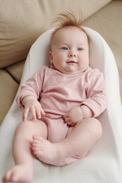 Adorável bebê com roupas rosa relaxando em uma pequena cama branca e macia