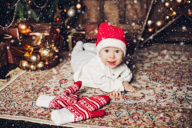 Adorável bebê feliz no chapéu vermelho no tapete com luvas de inverno bonito.