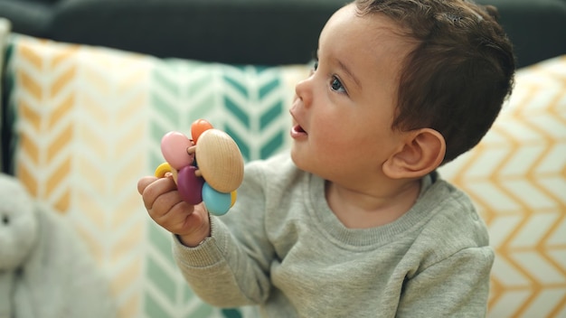 Adorável bebê hispânico chupando chupeta sentado na cama em casa