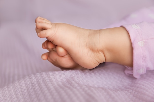 Foto adorável bebê minúsculo pernas em tecido lilás, closeup de pés infantis