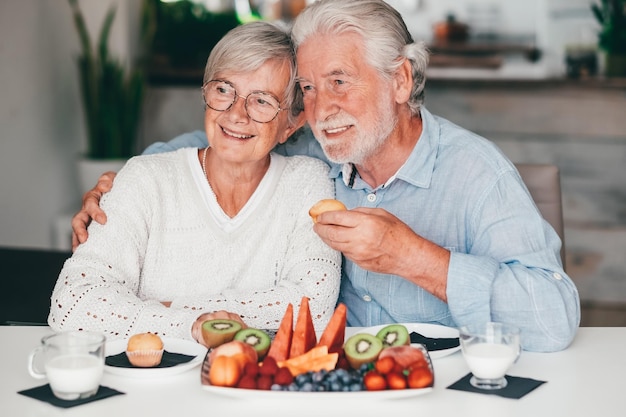 Adorável casal sênior sorridente em casa tomando café da manhã junto com leite de muffin e conceito de alimentação saudável de frutas frescas da estação