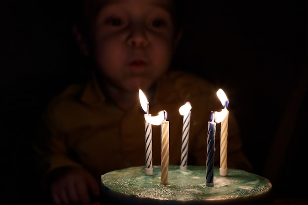 Adorável criança de cinco anos comemorando seu aniversário e soprando velas em bolo caseiro, interior. Festa de aniversário para crianças. Infância despreocupada, aniversário, felicidade.