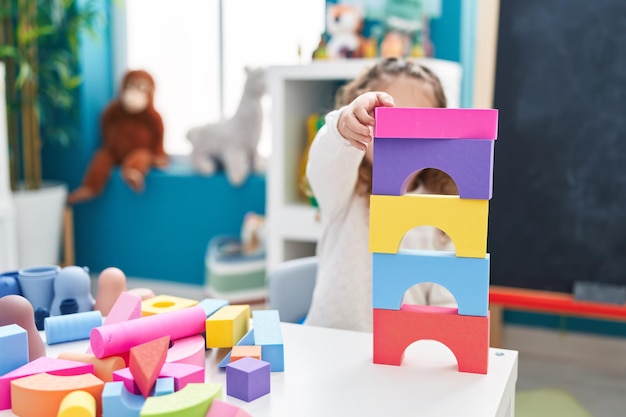 Adorável criança loira brincando com blocos de construção em pé no jardim de infância