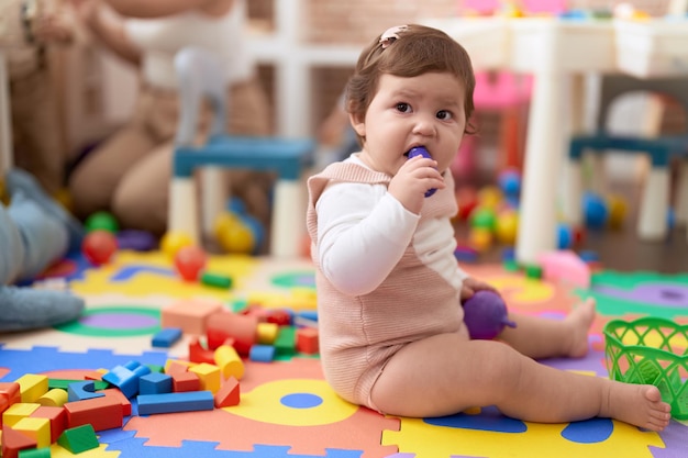 Foto adorável criança mordendo brinquedo de comida de plástico sentado no chão no jardim de infância