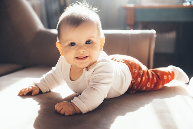 Adorável criança recém-nascida sorrindo para a câmera enquanto está deitada no sofá em um dia ensolarado