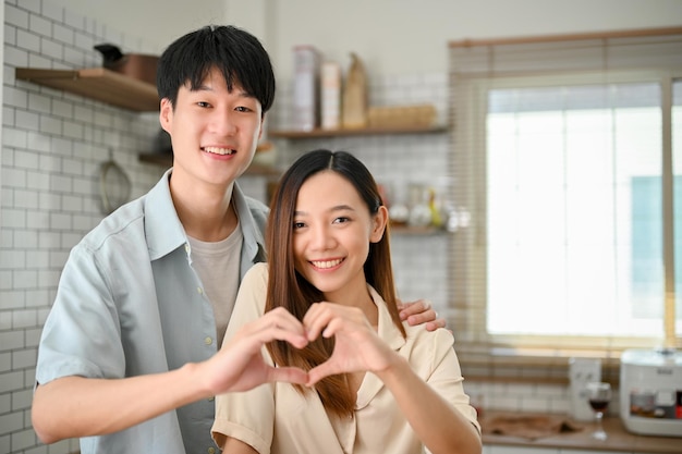 Adorável e apaixonado jovem casal asiático fazendo um sinal de coração juntos na cozinha