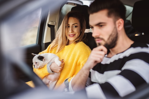 Adorável empresária moderna e sorridente segurando um cachorrinho fofo e olhando para um motorista de carro.